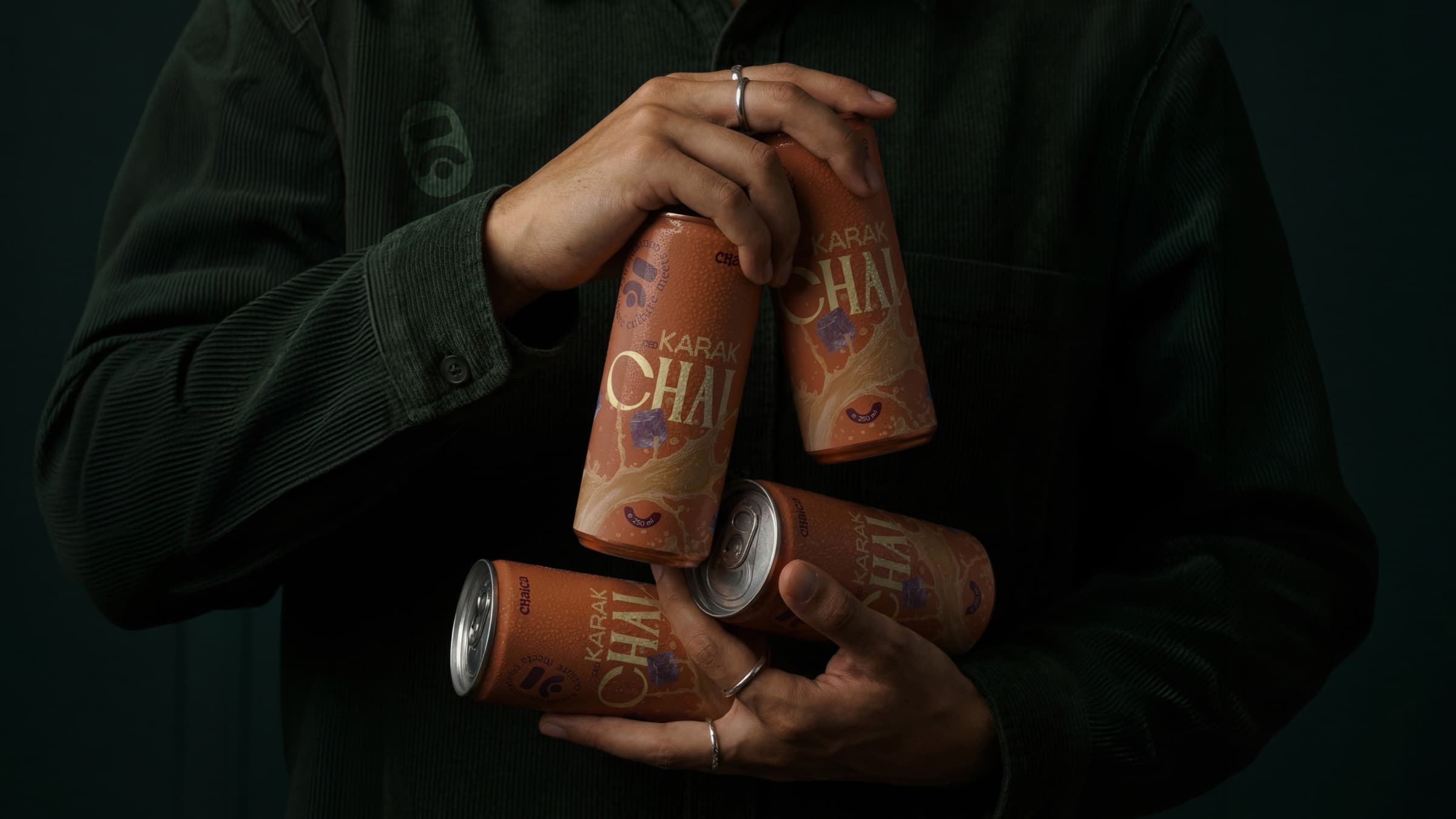 Hands holding four burnt-orange Chaico Karak Chai cans